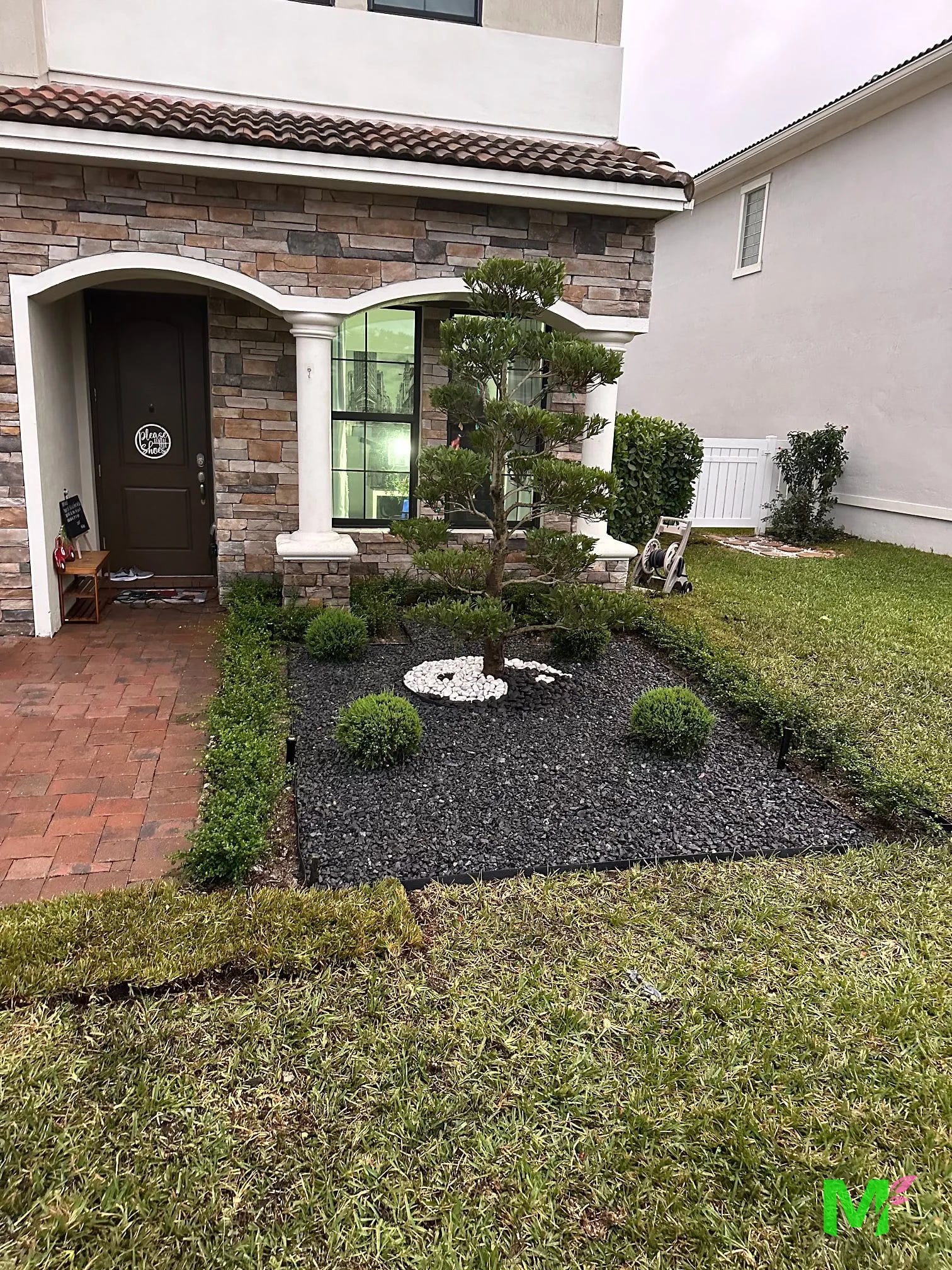 Entry bed finished with black rock, white stones, rounded shrubs and a clipped border