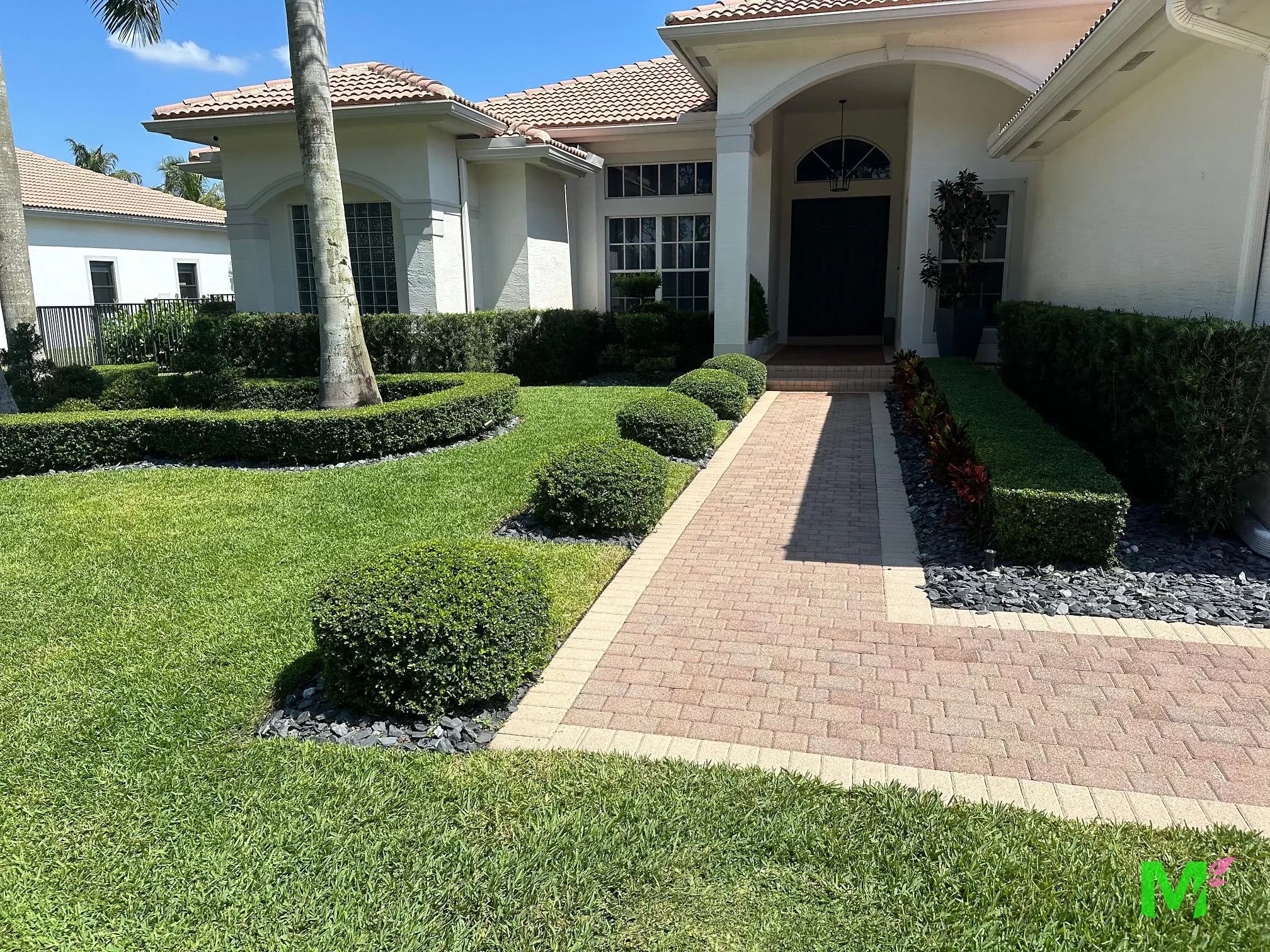 Brick paver walkway to a front entry, with rounded shrubs, clipped hedges and a manicured lawn