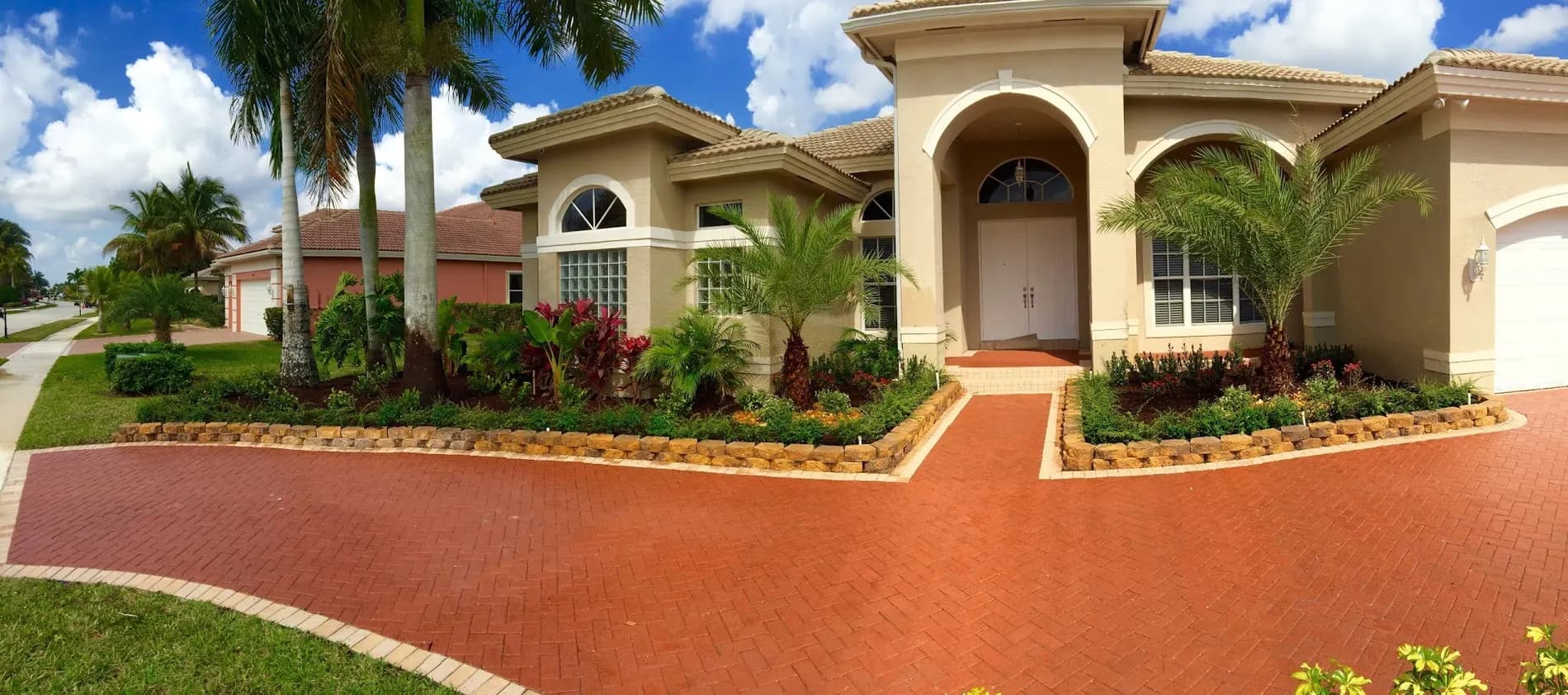 Large single-family estate with a brick paver circular drive, stone-edged planting beds and mature palms