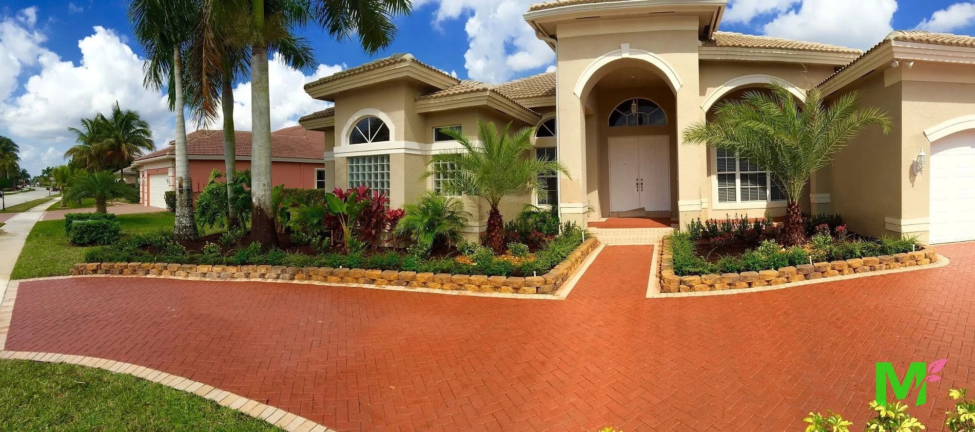 Large single-family estate with a brick paver circular drive, stone-edged planting beds and mature palms