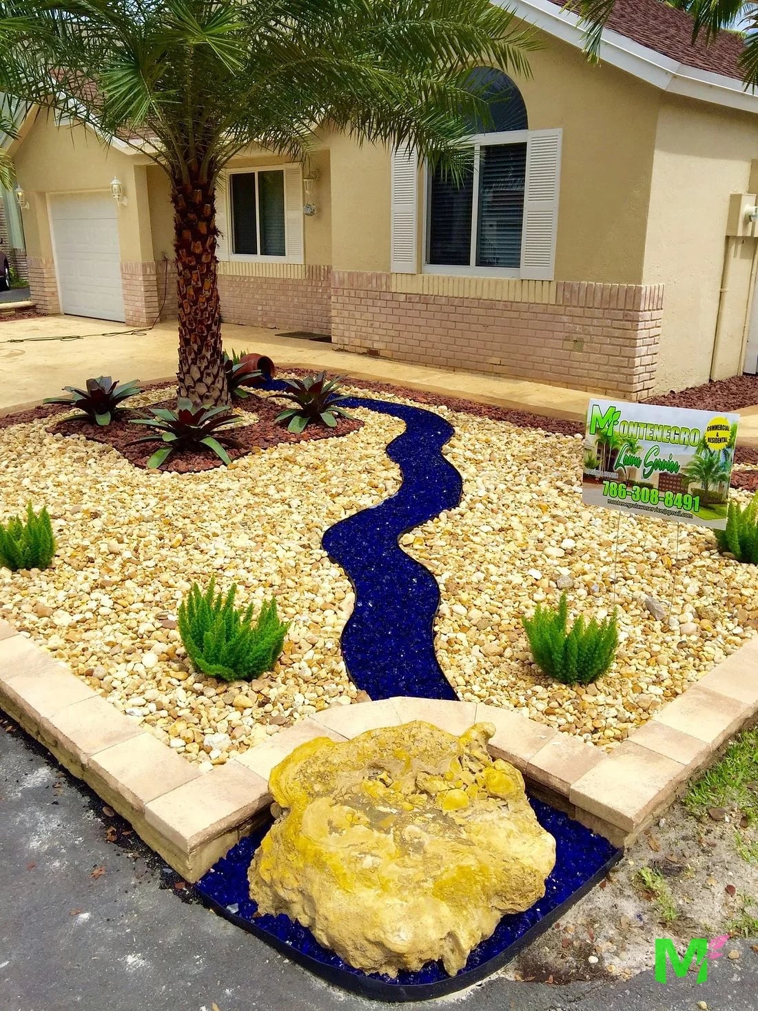 Xeriscape bed with a cobalt glass dry creek, bromeliads and a Montenegro Lawn Service yard sign