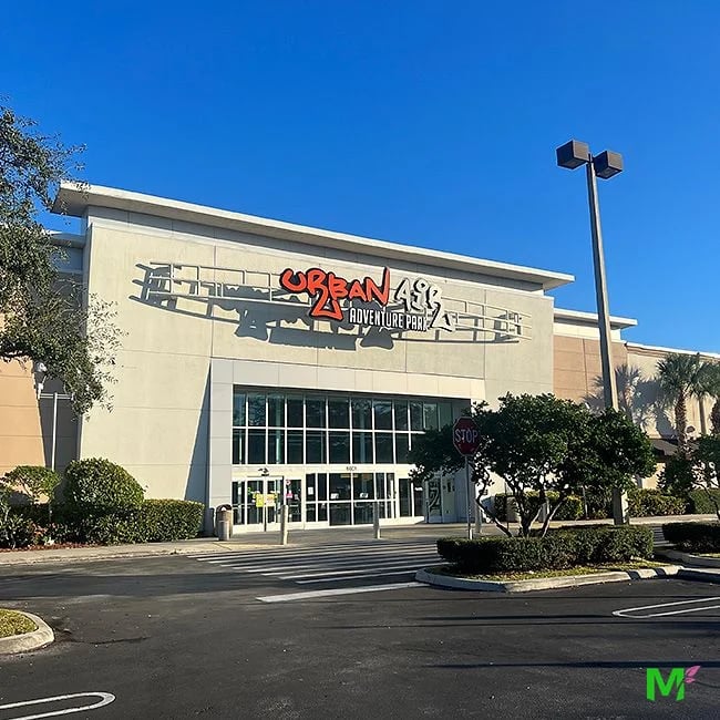Commercial plaza entrance with maintained hedges and shade trees